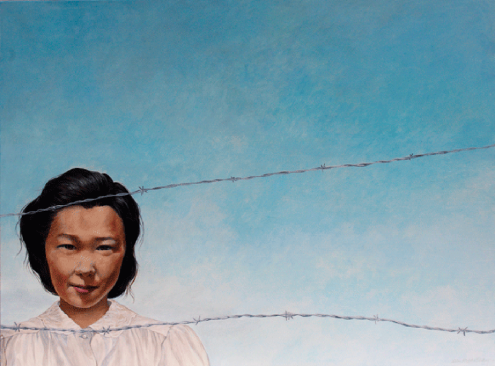 A Japanese Canadian woman stands behind barbed wire lines in front of a bright blue sky.